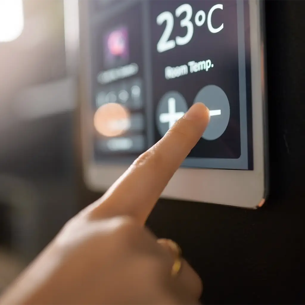 Eine Hand berührt das Display eines Smart-Home-Thermostats, um die Raumtemperatur auf 23 °C zu regeln.