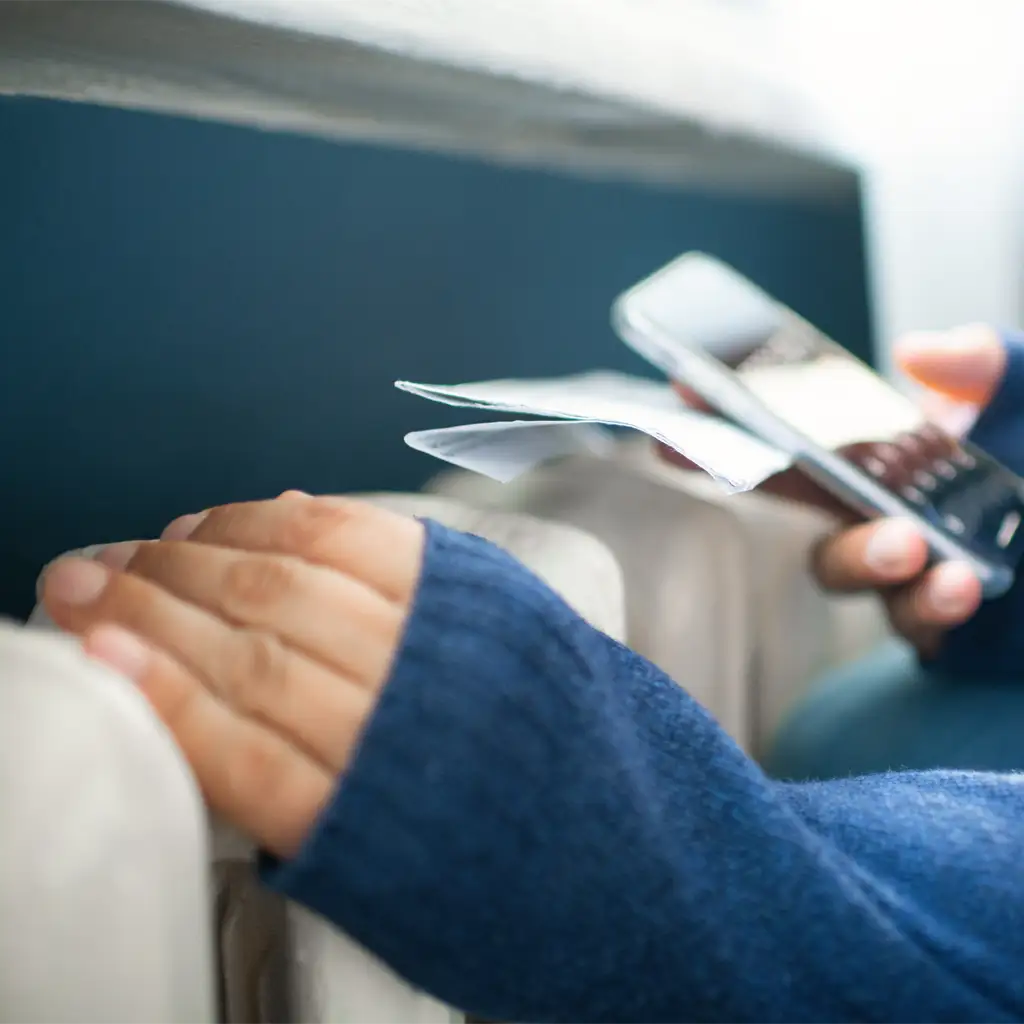 Eine Person überprüft Heizkostenabrechnungen mit einem Smartphone, während die Hand auf einem Heizkörper ruht.