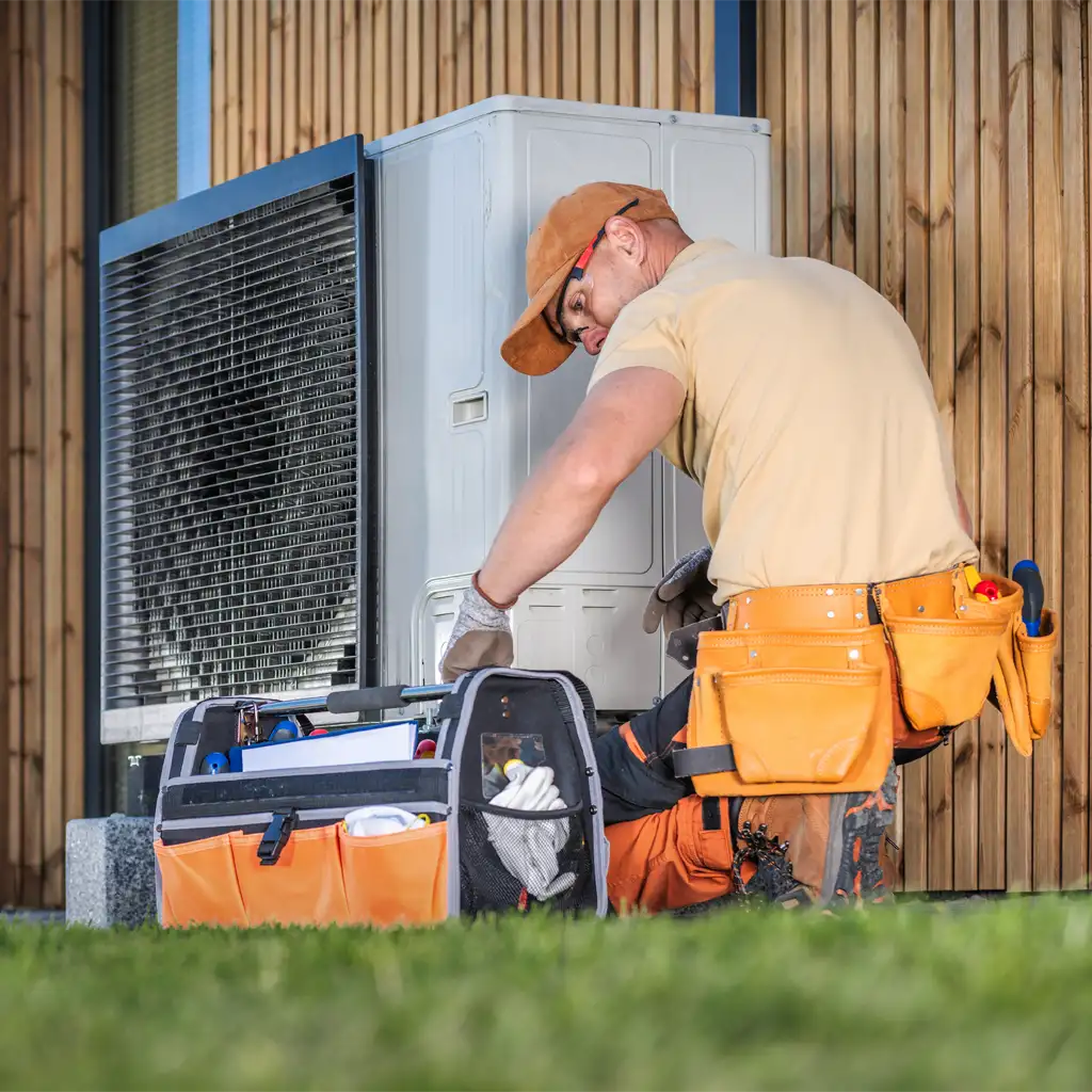 Fachgerechte Wartung einer Wärmepumpe: Techniker in Arbeitskleidung wartet eine Wärmepumpe oder Klimaanlage an der Außenwand eines modernen Gebäudes mit Holzverkleidung.